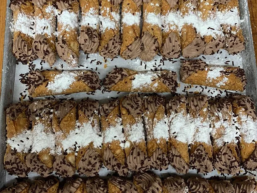Rows of cannoli filled with chocolate cream, dusted with powdered sugar and chocolate sprinkles