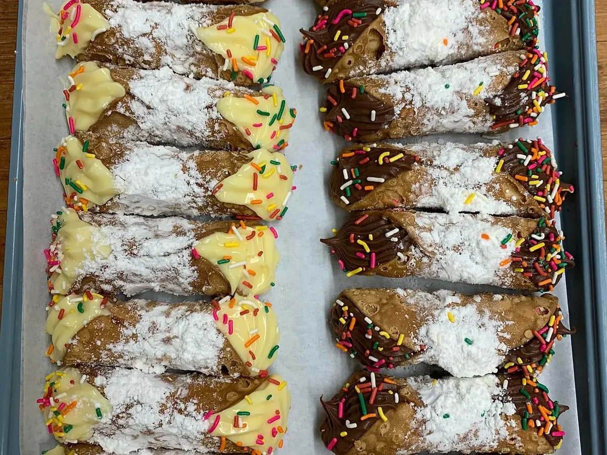 A tray of cannoli, one row filled with vanilla cream and one with chocolate, the ends dipped in rainbow sprinkles