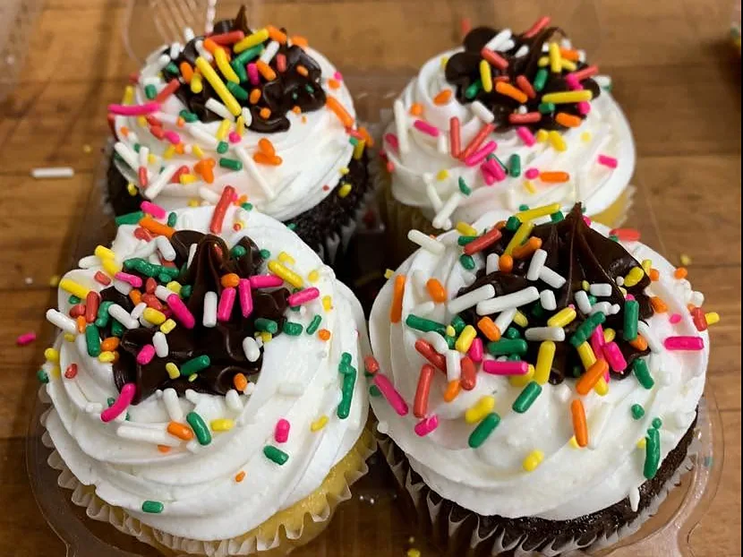 Four vanilla and chocolate cupcakes with white frosting, a swirl of chocolate and rainbow sprinkles