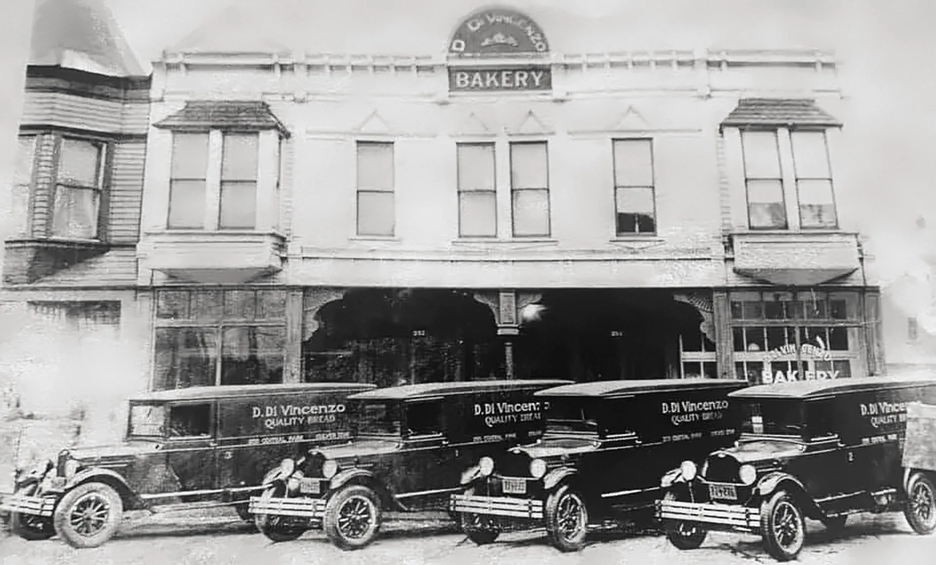 An old black-and-white photograph of D. Di Vincenzo Bakery, with four Quality Bread delivery trucks parked out front