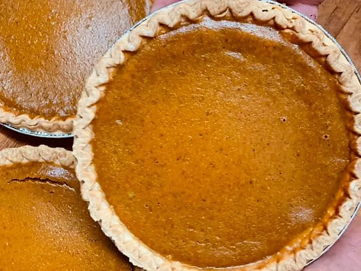 Pumpkin pies on a wooden counter, one held up in a hand