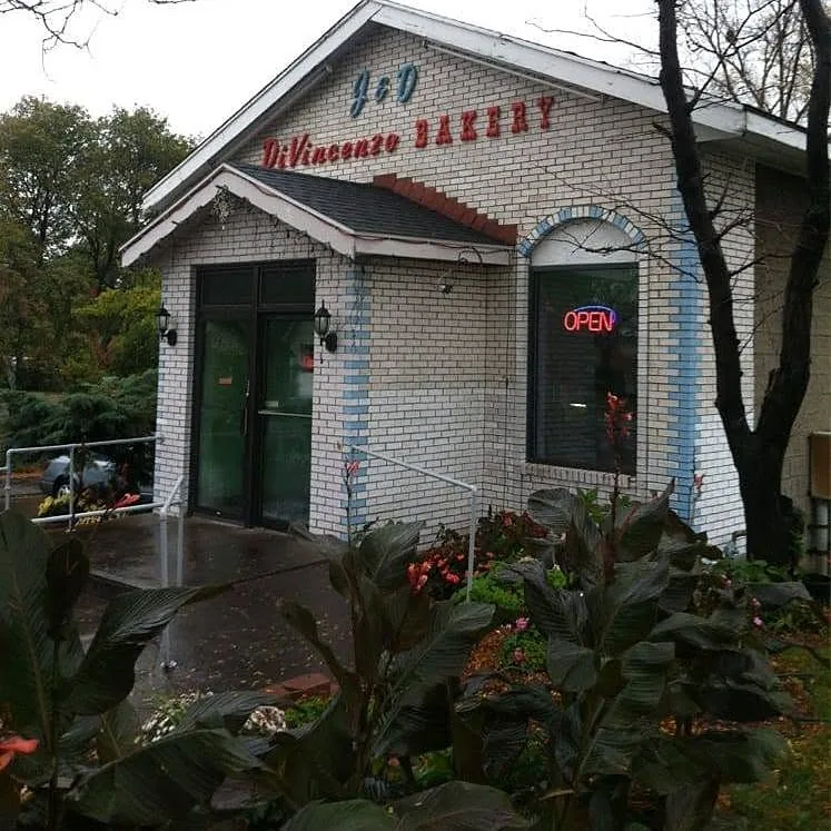 The J & D DiVincenzo Bakery shop: white brick with blue trim, a ramp to the door and an Open sign in the window